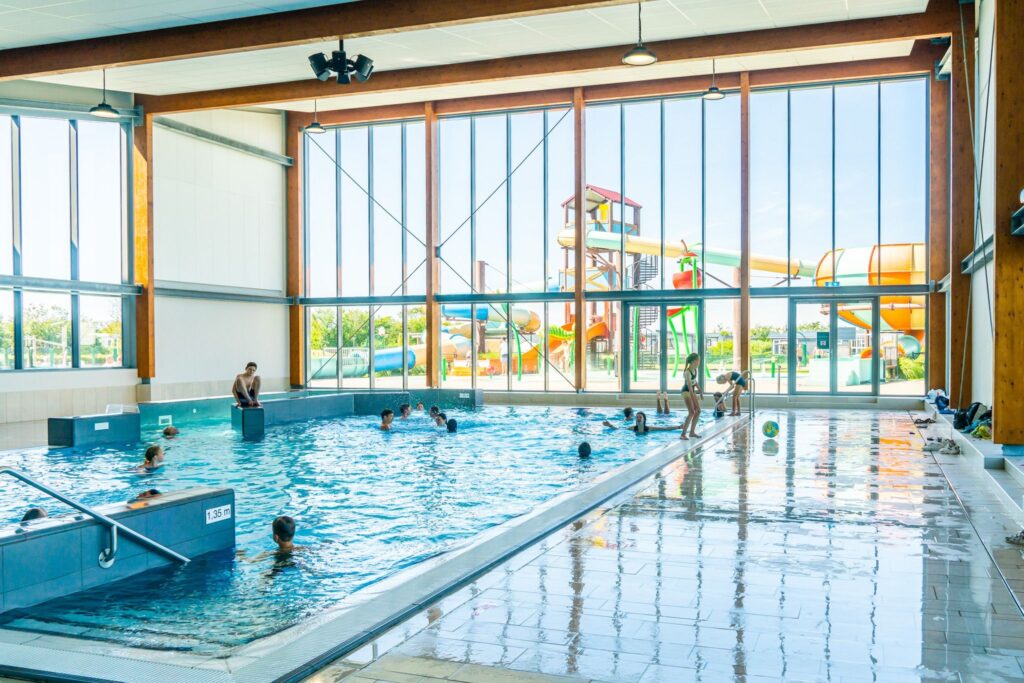 Kinderen en volwassenen zwemmen in een licht zwembad met uitzicht op glijbanen en zonnig weer in Westkapelle, Zeeland.