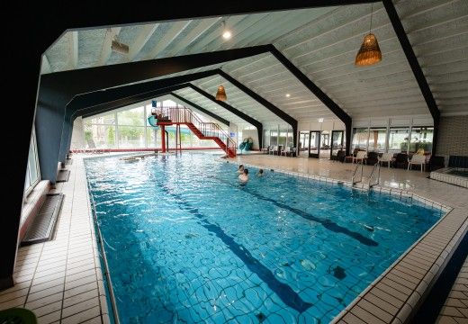 Binnenzwembad met rode glijbaan, zwemmers, grote ramen, zitplekken en balkenplafond in Overijssel.