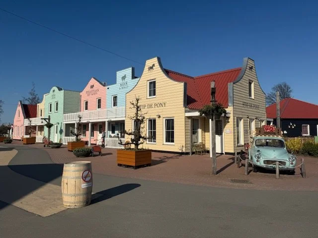 Kleurrijke westerse gebouwen langs een rustige straat bij Familie Resort Molenwaard, vintage auto en ton met rookverbod.