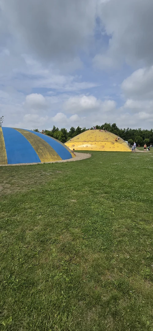 Twee grote, heuvelvormige speeltoestellen staan op het gras bij Camping De Kolibrie, met mensen die erop klimmen.