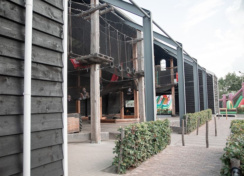 Houten klimtoestellen, touwnetten en bandenschommels in de deels omheinde speeltuin bij Klok'uus, Zeeland.