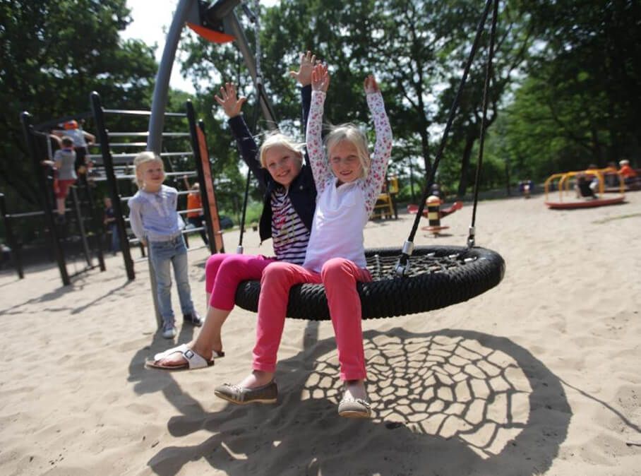 Twee lachende meisjes op een grote touwschommel in speeltuin Schatgraven Lutterzand, Overijssel; kinderen op de achtergrond.
