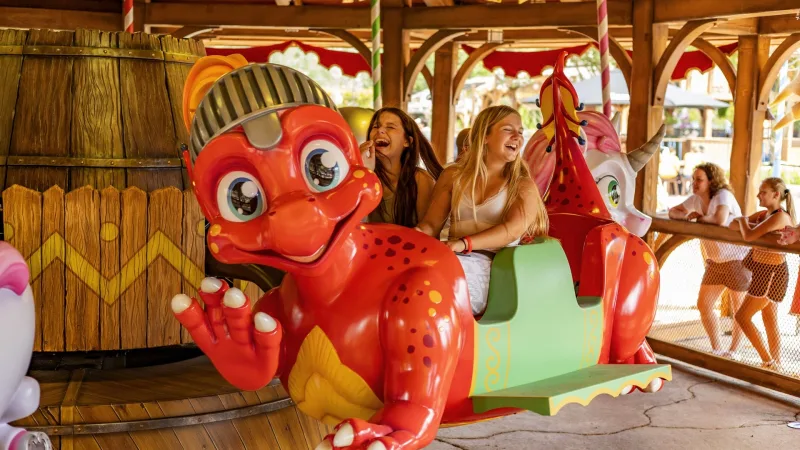 Twee jonge vrouwen lachen op een kleurrijke rode draak tijdens een attractierit in Toverland, Sevenum, Limburg.