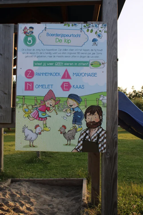 Bord bij speeltuin Camping De Kolibrie met tekeningen van kinderen, kippen, man en vraag over eieren in gerechten.