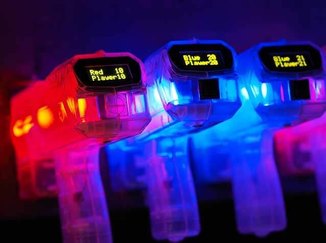 Drie transparante laserguns bij Dinoland Zwolle, Overijssel, verlicht met rood en blauw, liggen in een rij met scoredisplays.