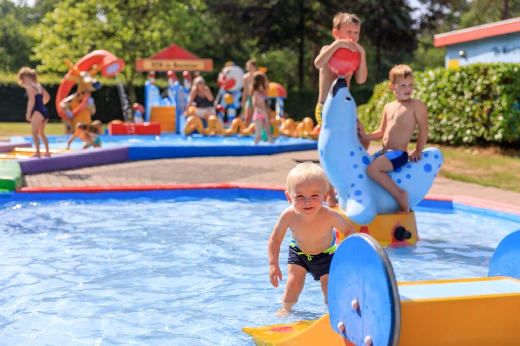 Kleine kinderen spelen in een ondiep buitenbad met watertoys en dierglijbanen bij RCN de Noordster, Drenthe.