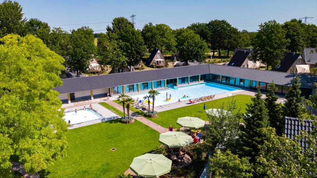 Kindvriendelijk modern openluchtzwembad op de Sallandse Heuvelrug, met zwemmers, grasvelden en omringende bomen.