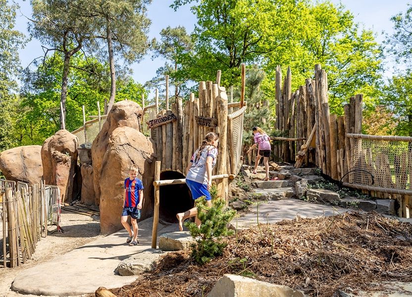 Kinderen spelen op de houten en rotsachtige avonturenspeeltuin bij Avonturenpark De Bergen, tussen bomen en groen.